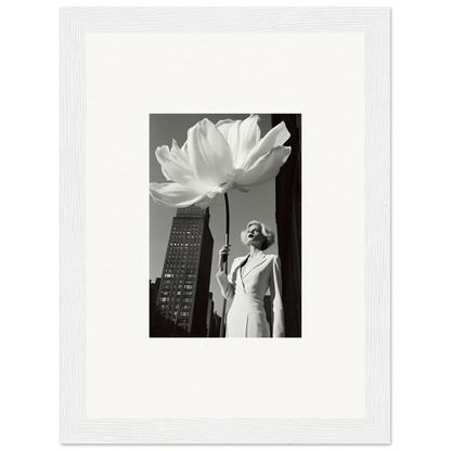 A framed black and white photograph showing a person standing next to an oversized flower against a cityscape backdrop.