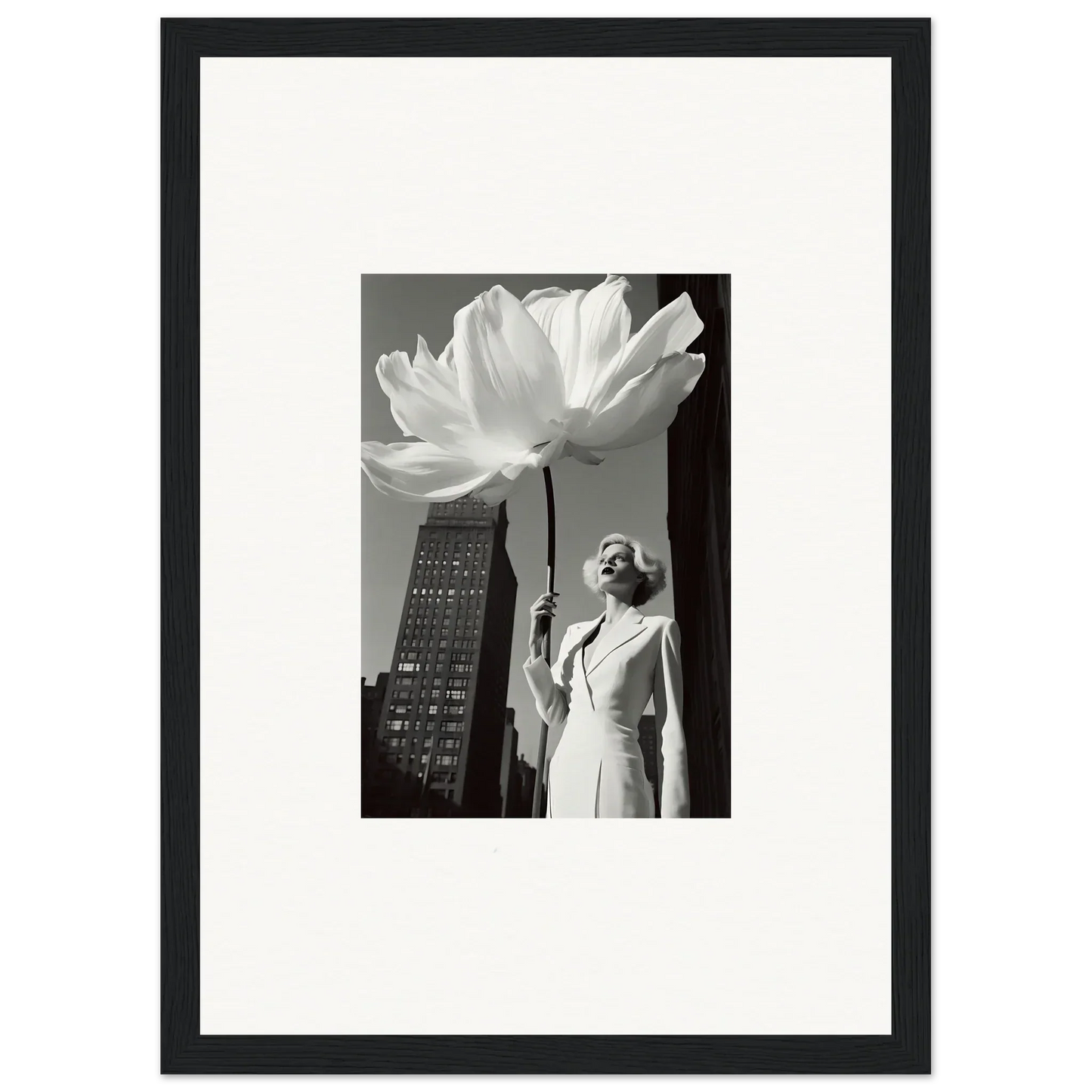 Black and white photograph of a woman standing next to an oversized flower in an urban setting.