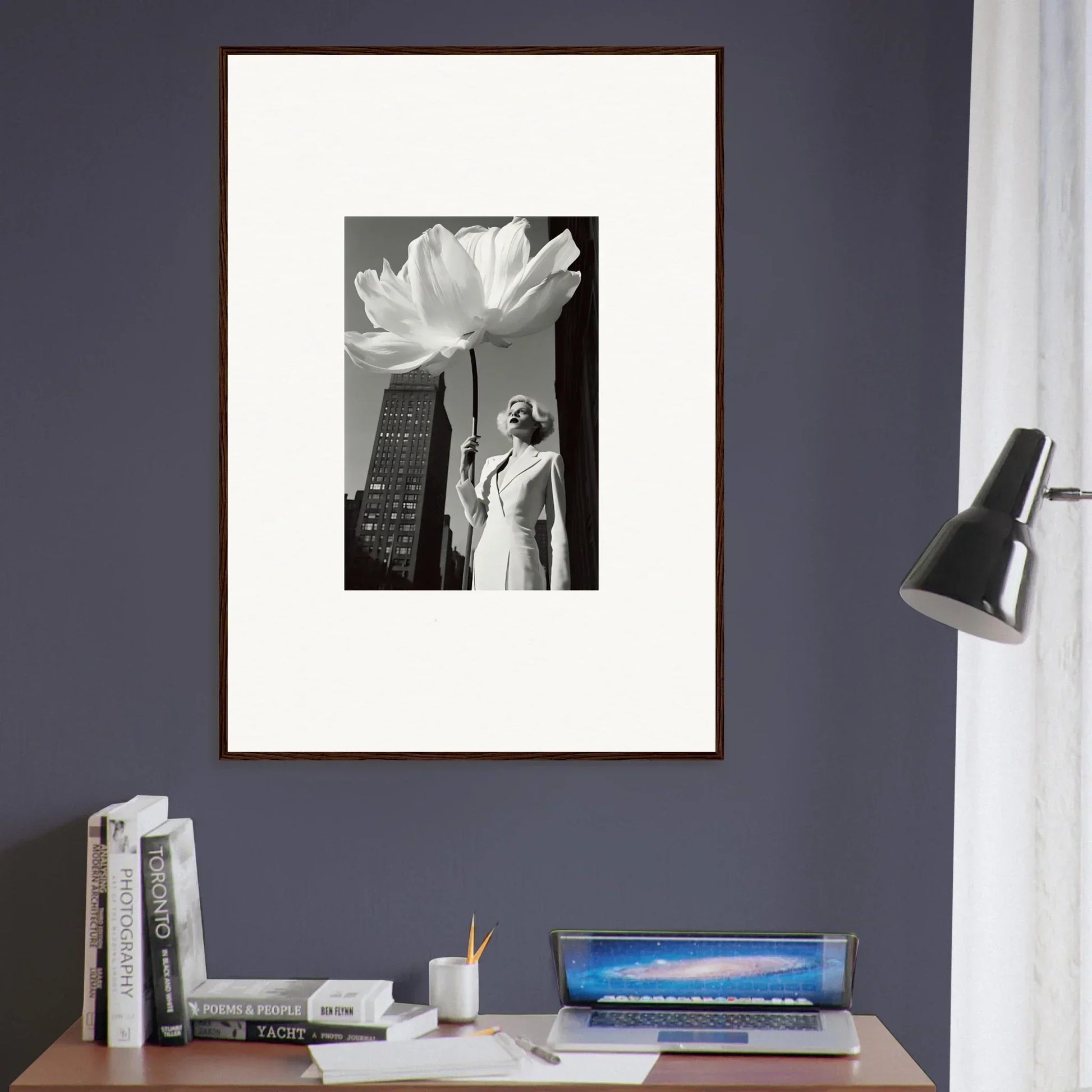 Framed black and white photograph of a person standing next to a giant flower with a city skyline in the background.