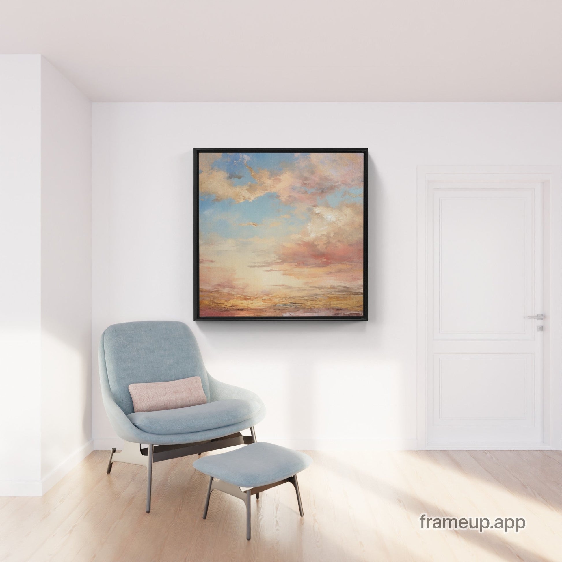 Framed sunset sky painting above a light blue armchair and matching footstool.