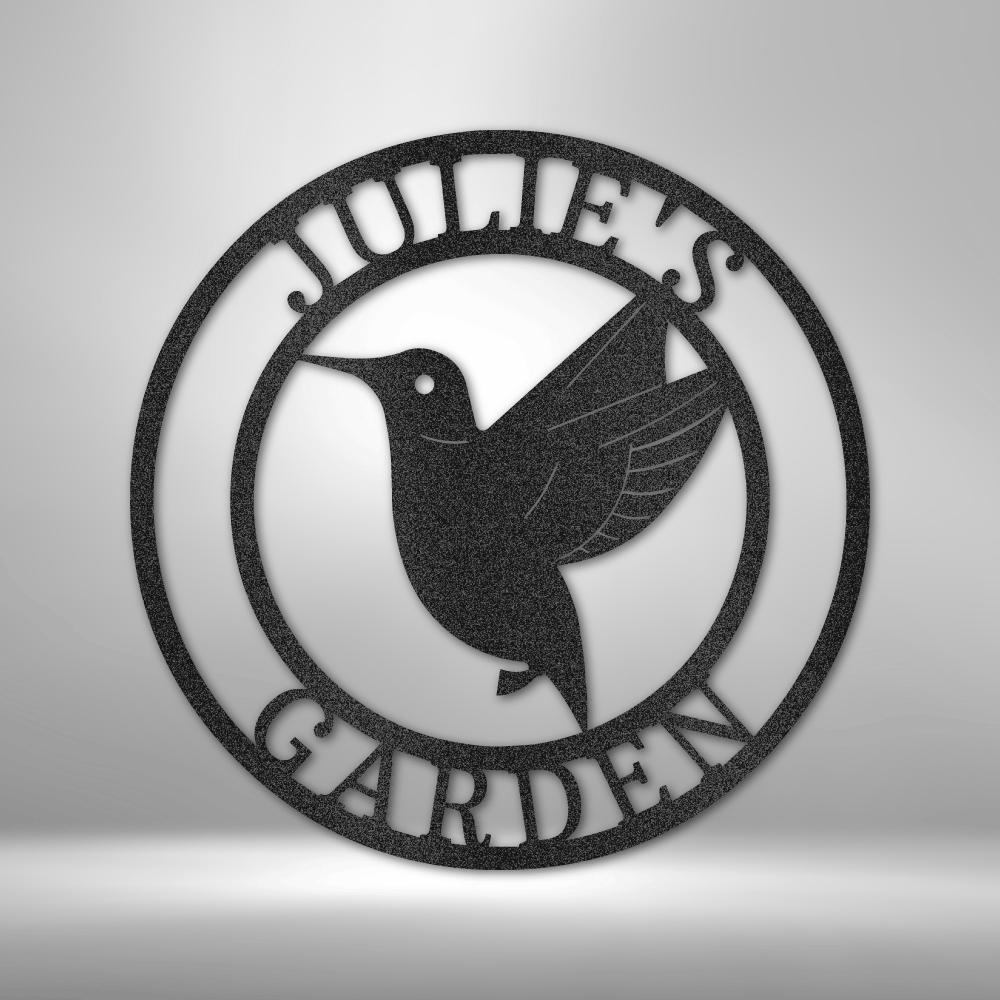 Circular metal sign featuring a hummingbird silhouette and the text ’JULIE’S GARDEN’.