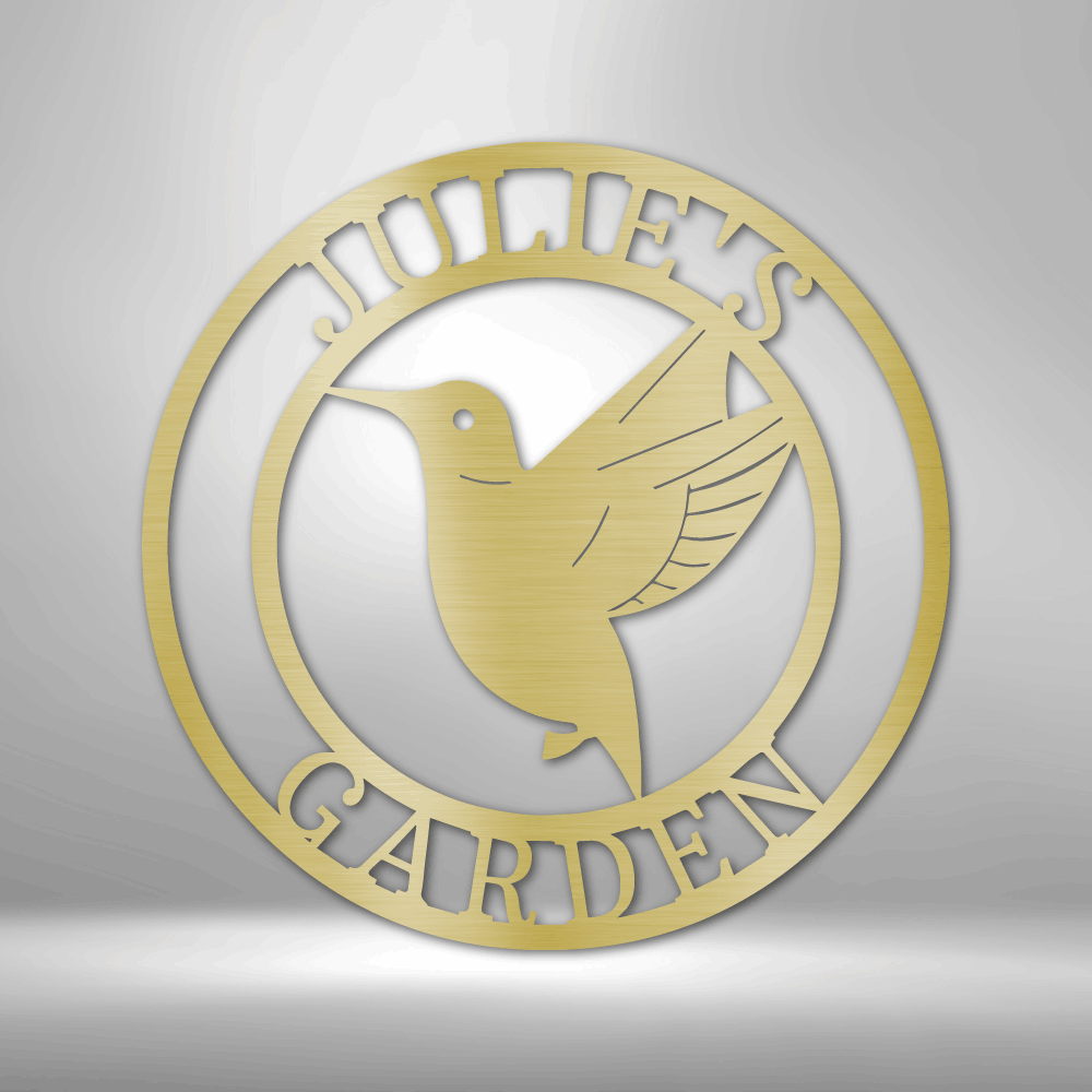 Circular gold-colored metal sign featuring a hummingbird design and the text ’JOHN’S GARDEN’.