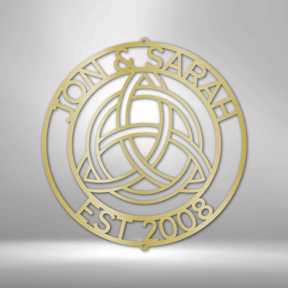 Circular gold-colored emblem featuring a Celtic trinity knot design and text ’JOAN & SARAH EST 2008’’.