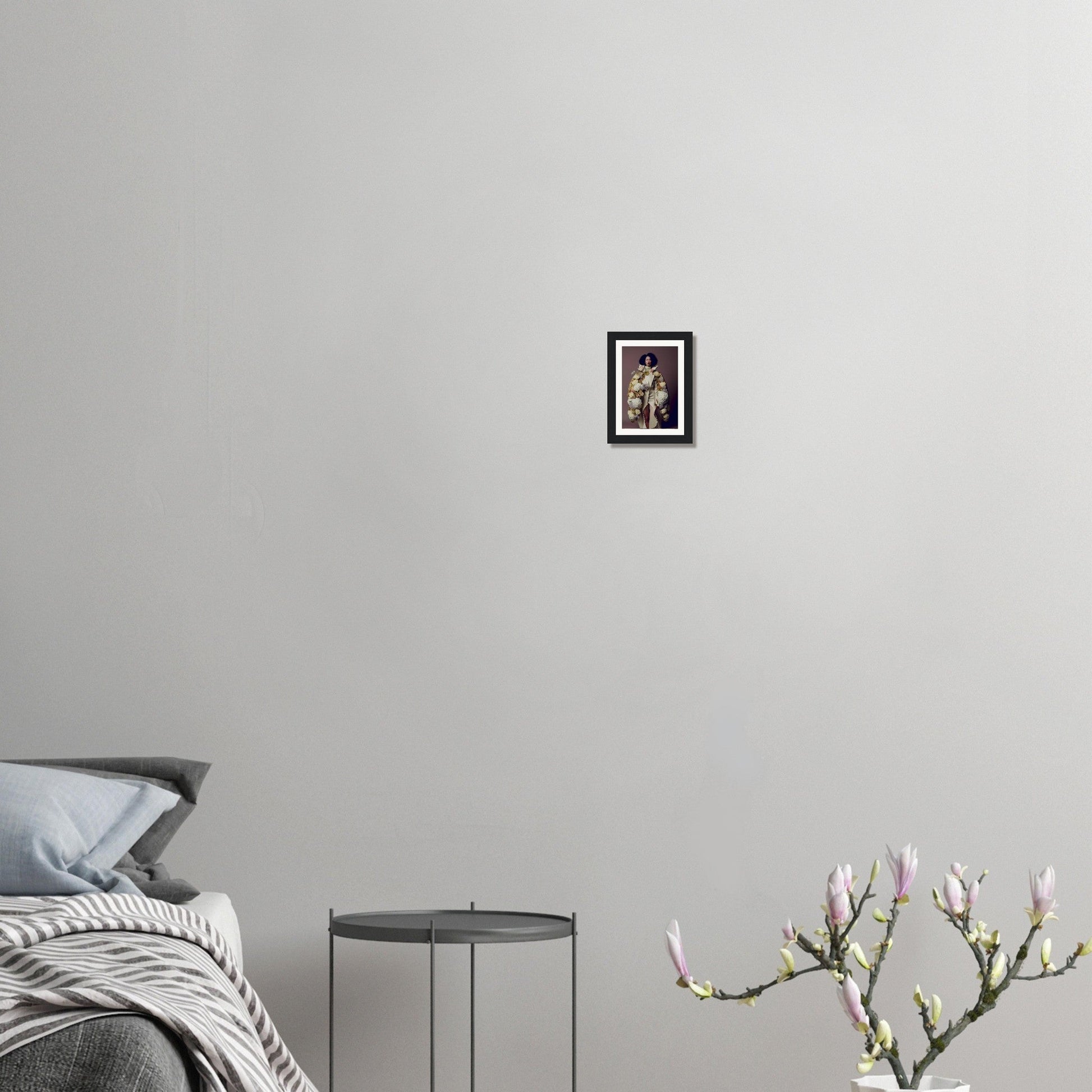 Minimalist bedroom with a bed, side table, framed artwork, and a flowering plant branch.